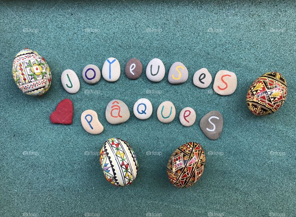 Joyeuses Pâques, french Happy Easter with carved and colored stones, traditional decorated eggs over green sand 