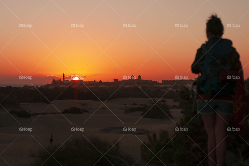 Girl is looking at the sunset on the sand dunes of Maspalomas, Gran Canaria, Canary Islands.