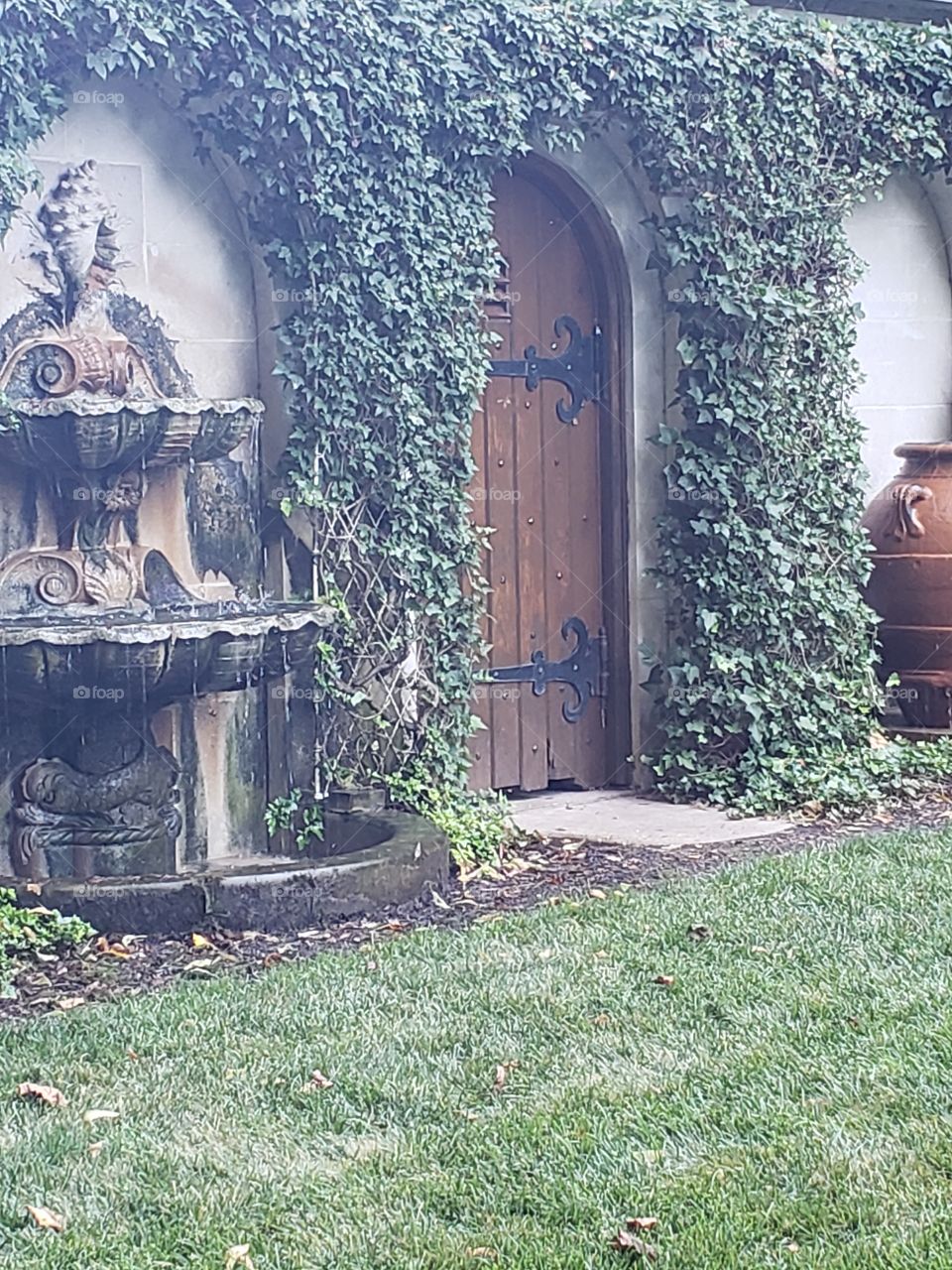 Old wooden door nestled between English Ivy arches and water fountains is reminiscent of the entrance to the secret garden