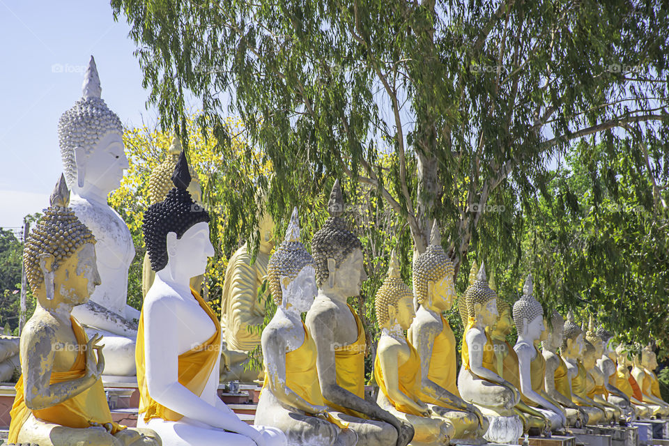 The statue of Buddha  covered in yellow cloth Background tree and sky at Wat Phai Rong Wua , Suphan Buri in Thailand.