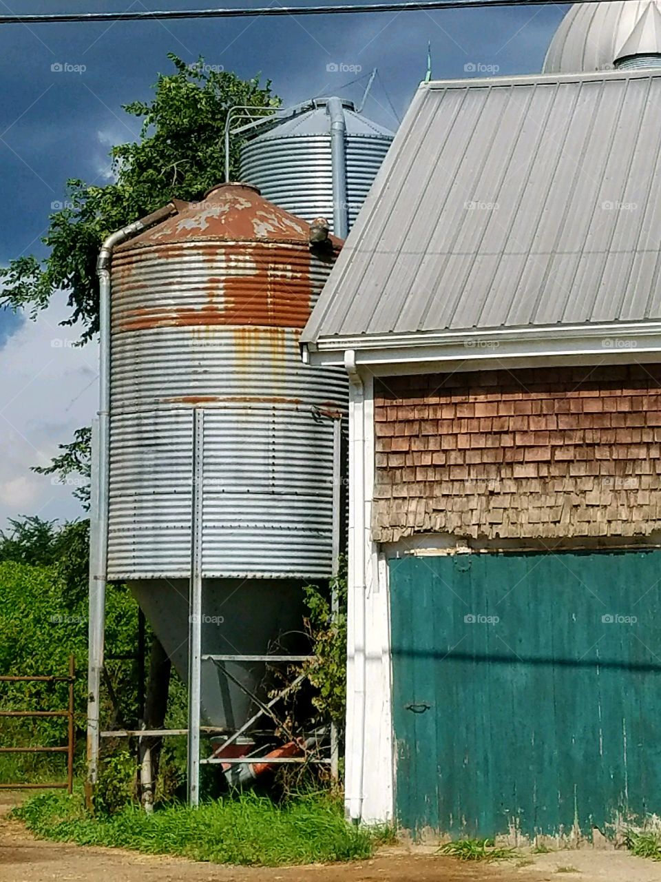 Large silo & end of barn. Dirt road to back field visible. Rusty silo.
