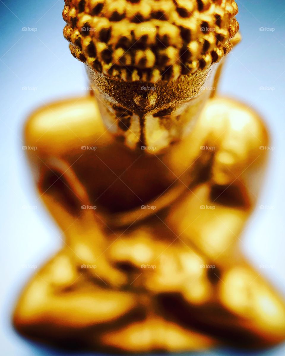 Macro photo of a golden tiny Buddha statue against a grey background, depicting Buddhism, meditation or spirituality 