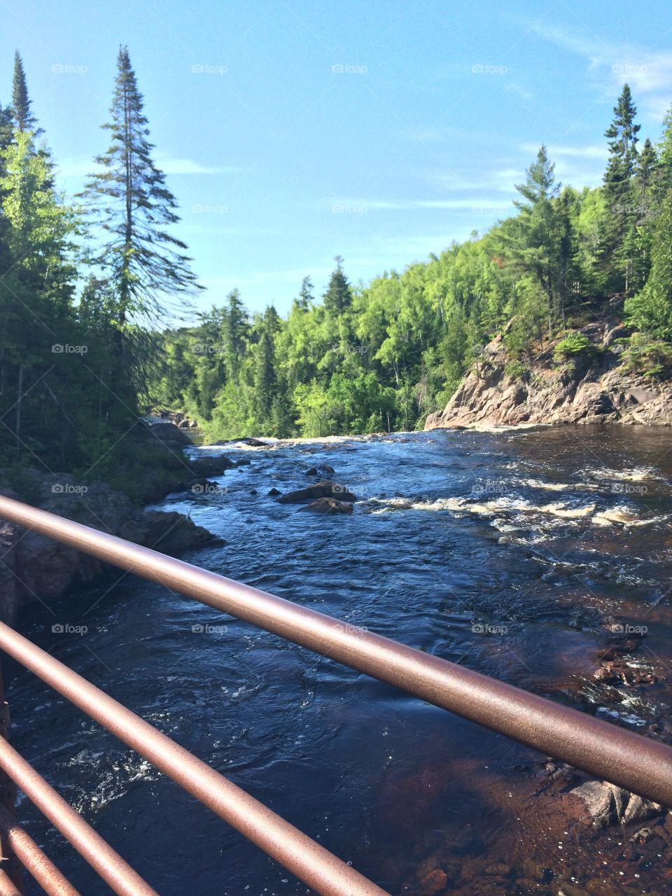 The river wild on a steel bridge, looking at evergreens, blue skies, and rocks