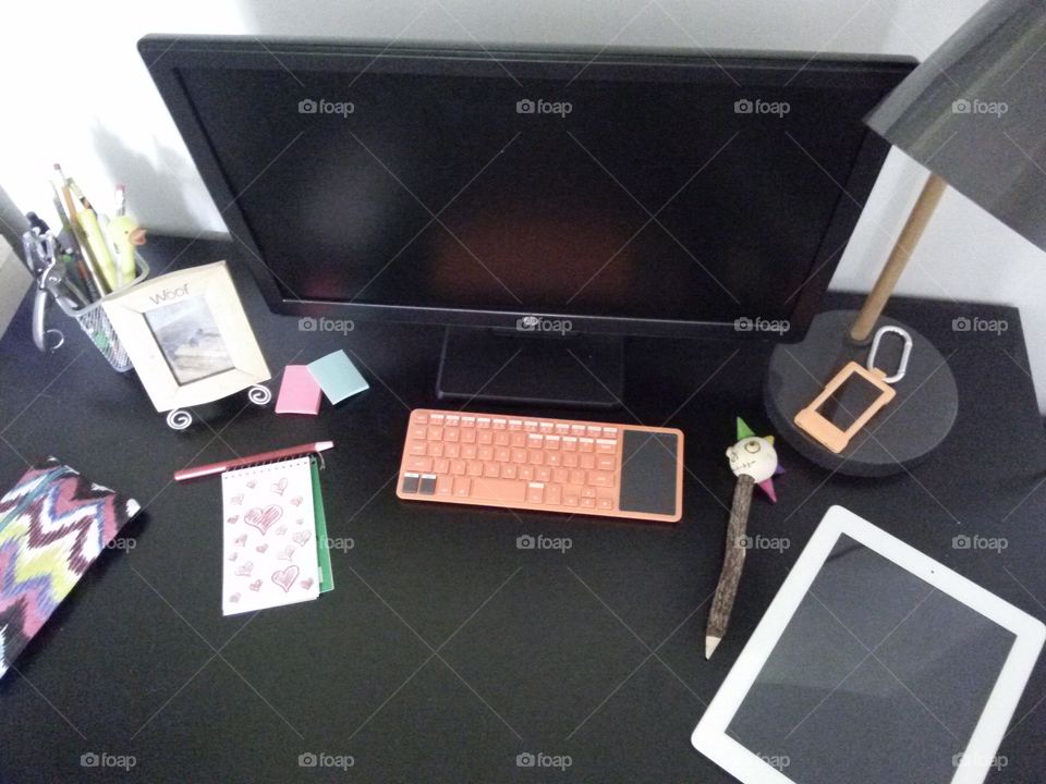 Desk, from above. work space: computer, doodle pad, photo frame, tablet, mp3 player, and misc supplies.