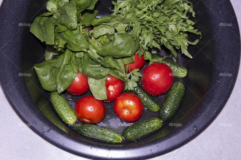 Fresh, green, vegetarian vegetables under the tap in a black sink for preparing salads and other dishes in a homely gray and green kitchen.