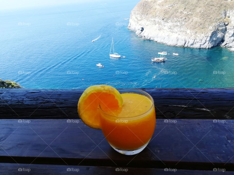 Orange juice in the foreground and the bay of Sorgeto (Italy) in the background