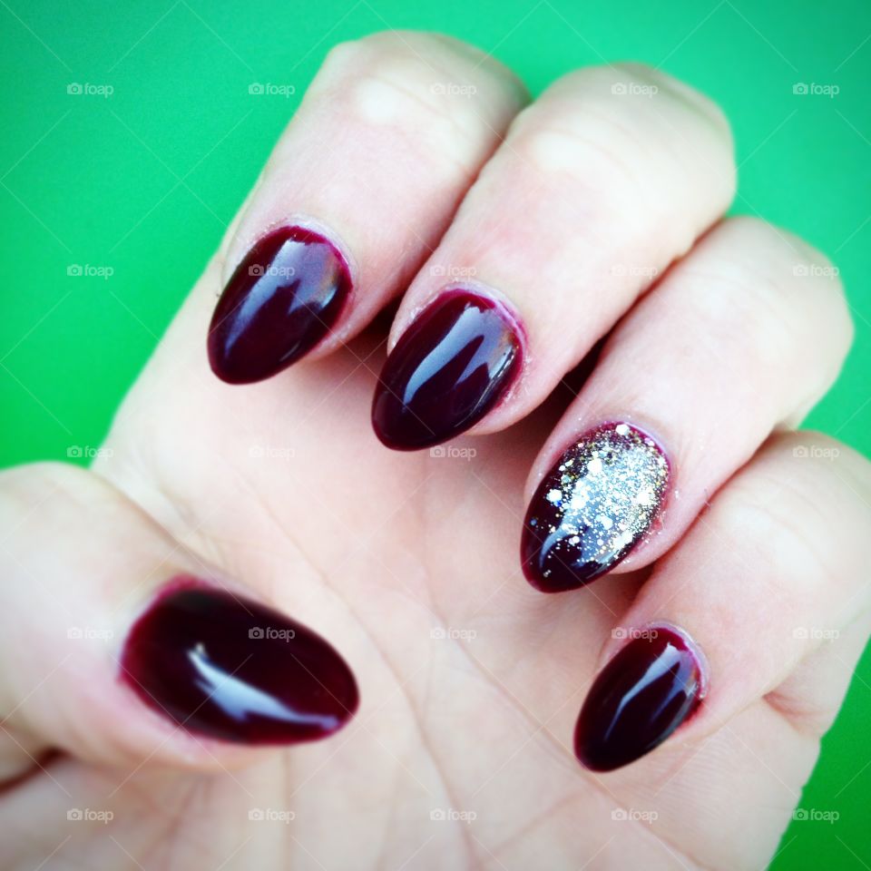 A nice set of burgundy nails with a sparkly accent nail against a green background. Merry Christmas to all.