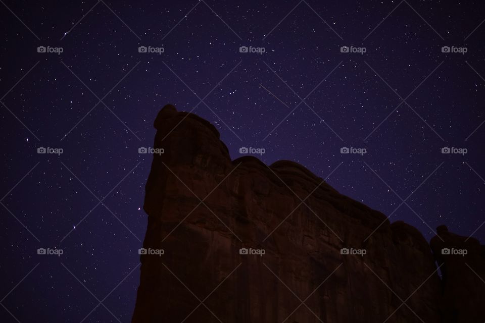Stars and a colorful night sky in Arches National Park on a clear spring night. Stars light up the sky. Shooting star is focus.