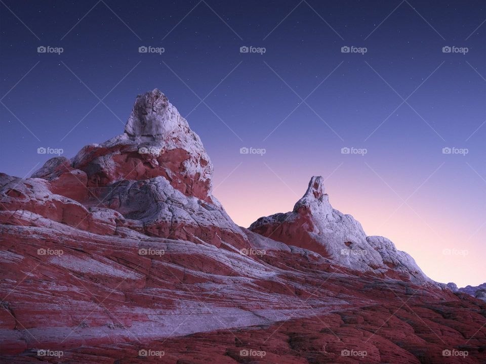 The sun sets as stars appear over unique rock formations