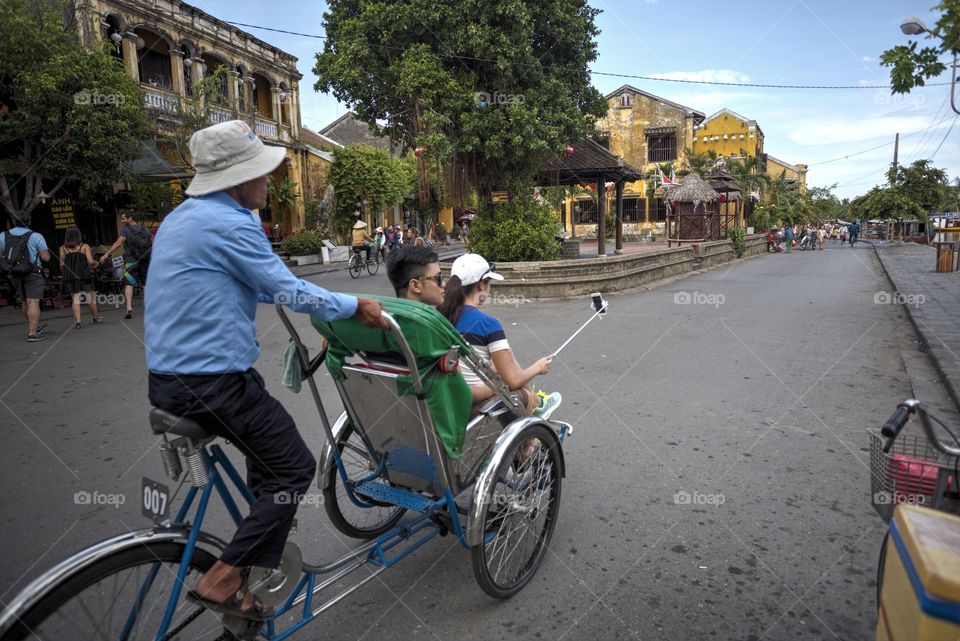 typical scene in Hoi An ancient town in central Vietnam. picturesque photo of taxi driver transporting tourist on a cyclo discovering the town