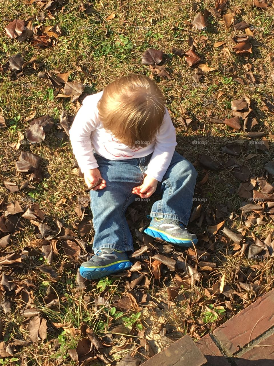 Baby sitting in grass with dead leaves.