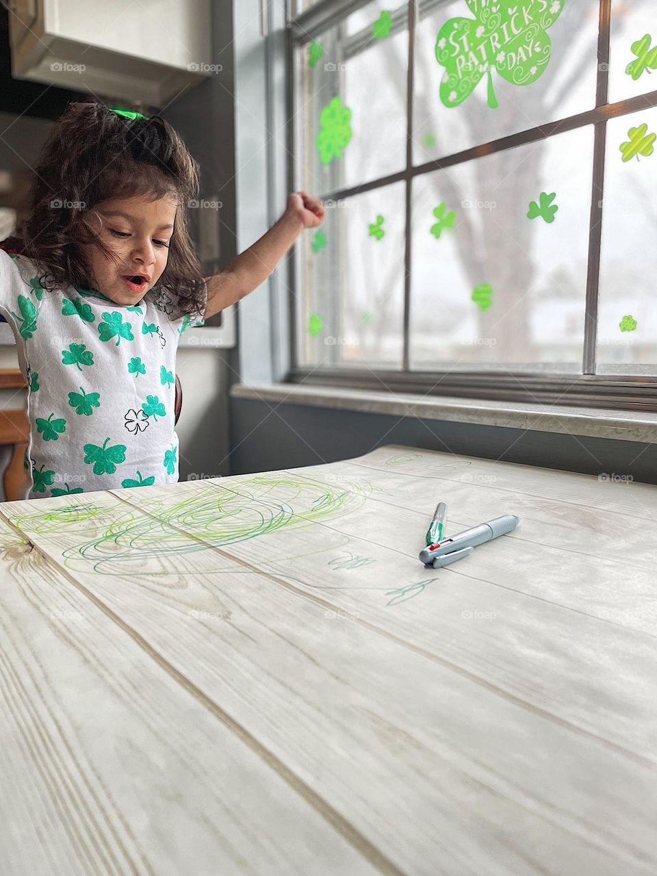 Toddler girl celebrates her success with coloring, toddler girl is excited by her accomplishments, toddler girl throws arms up to celebrate, self confidence in toddler girls, portraits of toddlers, St. Patrick’s Day outfit