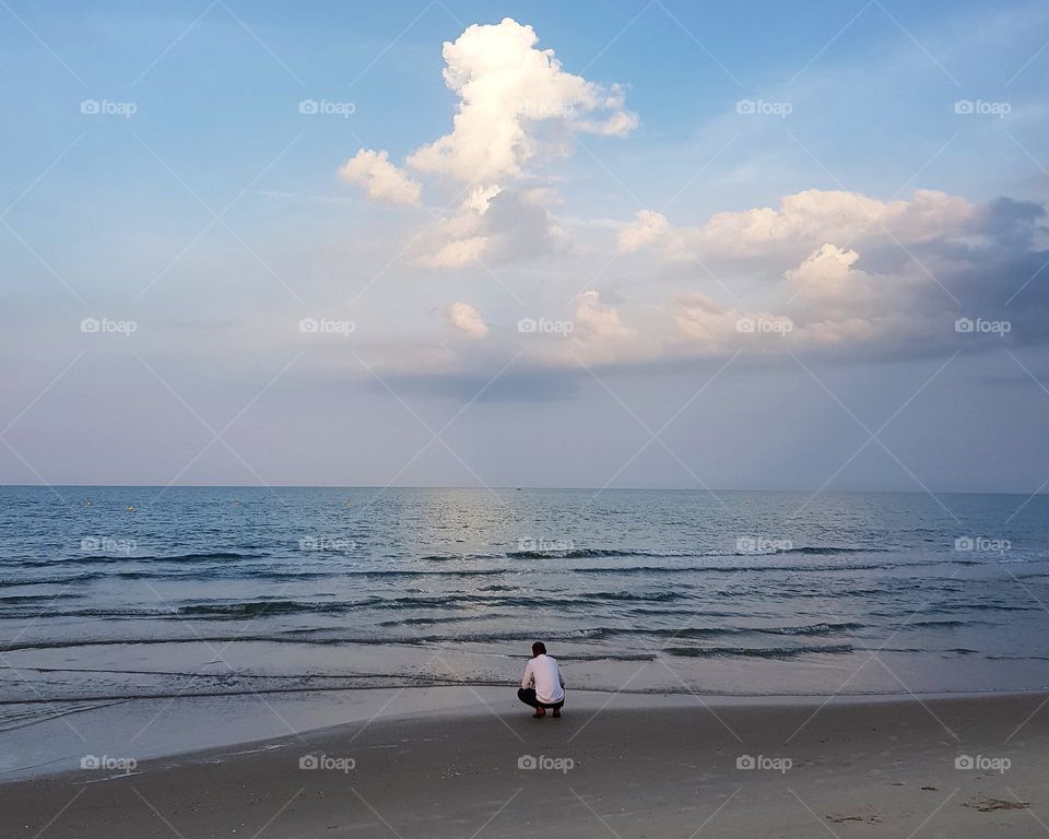 Man sitting on beach against blue sky