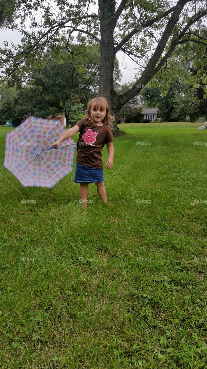 Little girl with umbrella playing in the garden