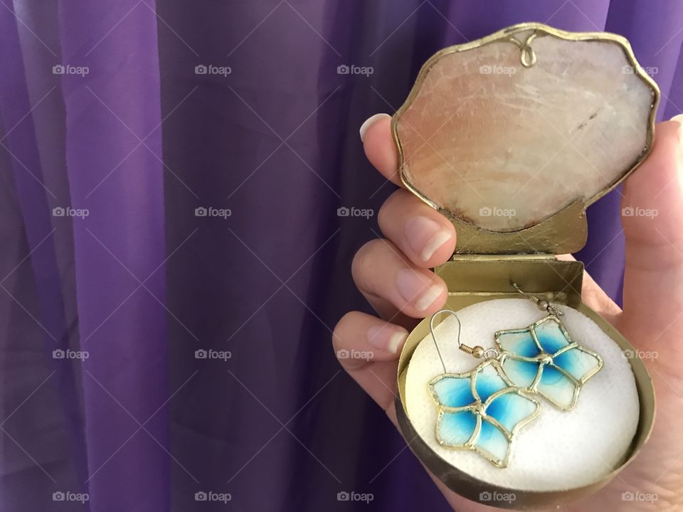 Female holding shell earrings in a shell case with a purple background