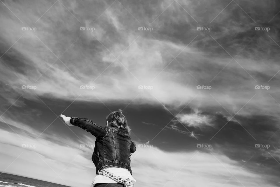 Girl in jeans jacket jumping against sky.