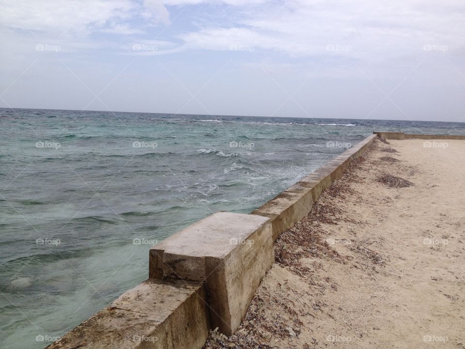 A beach front wall holds  the crashing waves back, keeping them from dampening the white sandy beach. 