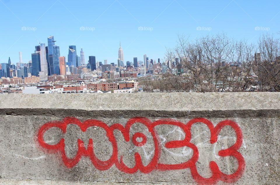 Graffiti tag “Mack” in red paint on wall with New York City skyline and blue spring sky in background 