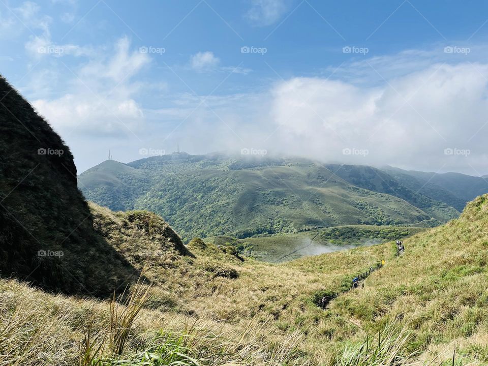 Photo of Qixing Mountain's scenic view: blue sky, green grassland, wildflowers, and magnificent mountain peaks shining in sunlight. A harmonious and beautiful natural landscape.