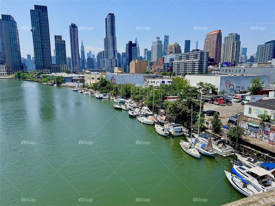 This gorgeous panorama unfolds overlooking “Newtown Creek” with its many boats from the “Pulaski Bridge” that connects “Greenpoint”, Bklyn to LIC. “Manhattan” including the “Empire State Bldg” is visible in the distance. 2024. Hypnotic Productions