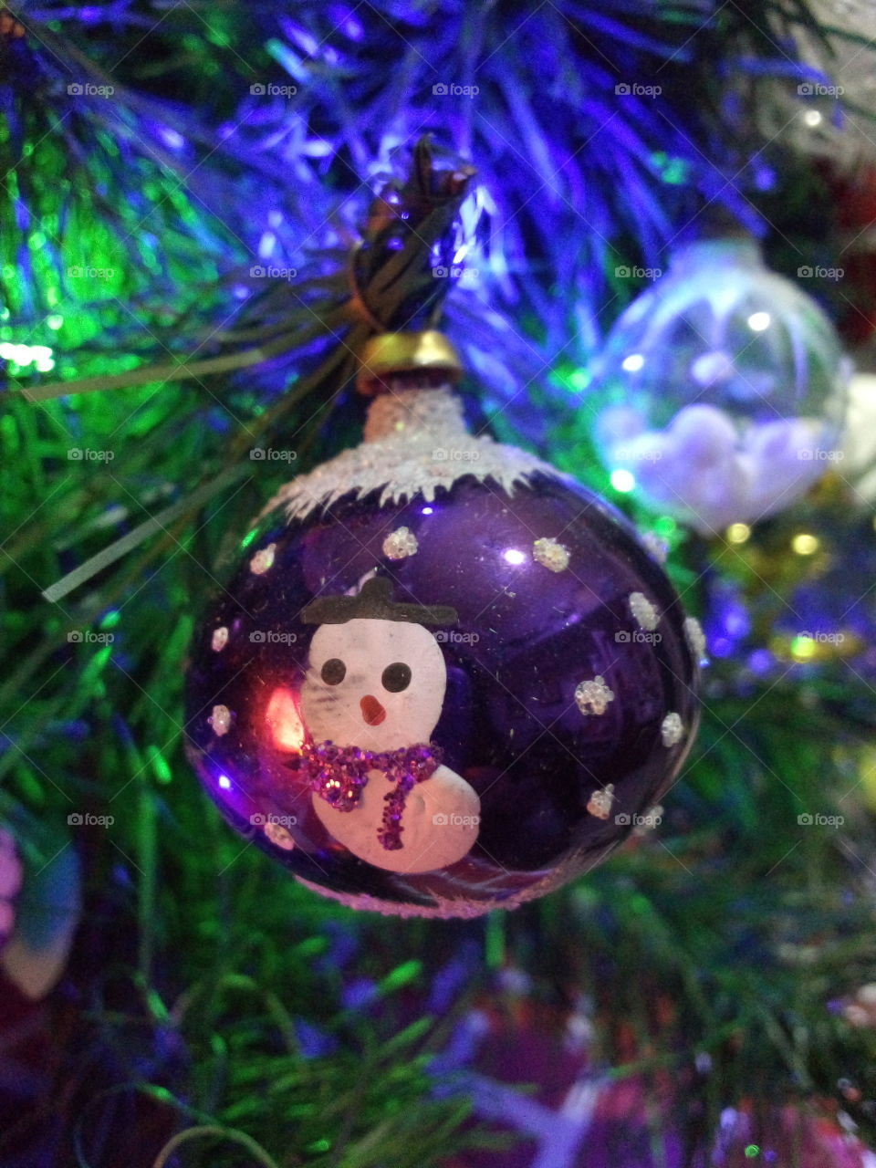 esfera de navidad en árbol con motivo de hombre hielo pintado a mano. En el fondo otra pequeña esfera con nieve dentro.