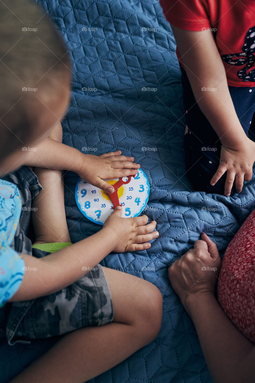 Kids learning how to tell time from clock and set the hands in the correct position. Teaching preschoolers tell time. Candid people, real moments, authentic situations