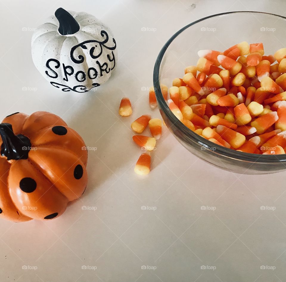 Candy corn in a dish surrounded by cute mini decorated pumpkins, getting ready for Halloween night. 