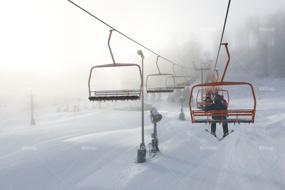 First rides on a ski lift early in the morning. Fog, haze, foggy weather. Downhill, slope skiing on fresh white snow