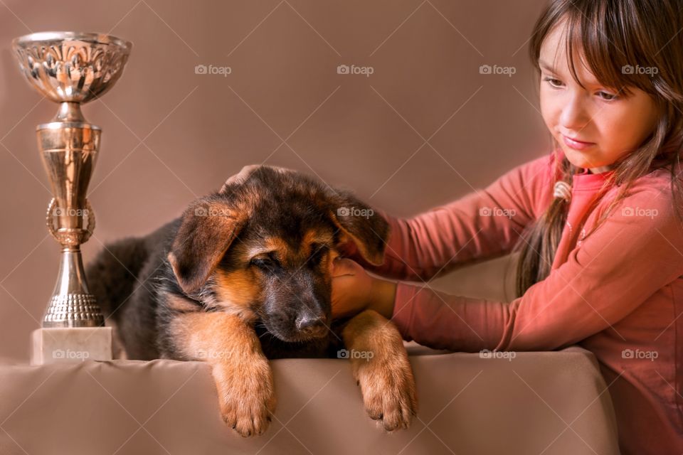 Little girl with German shepherd puppy on light brown background 