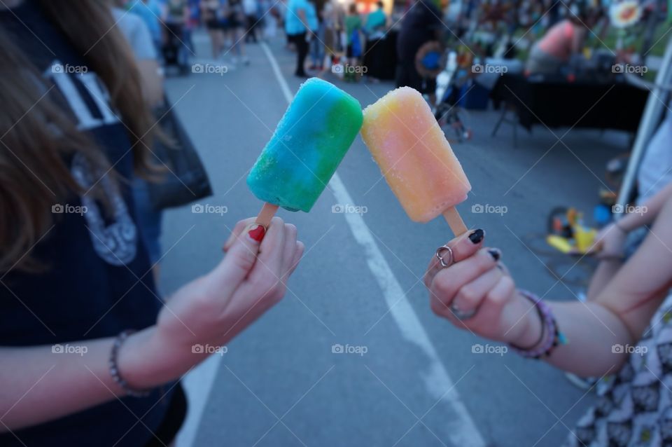 Friends and ice cream sticks. Photo taken in OK.  Two girls clinking  a toast with ice cream on a stick.  Summer fun!