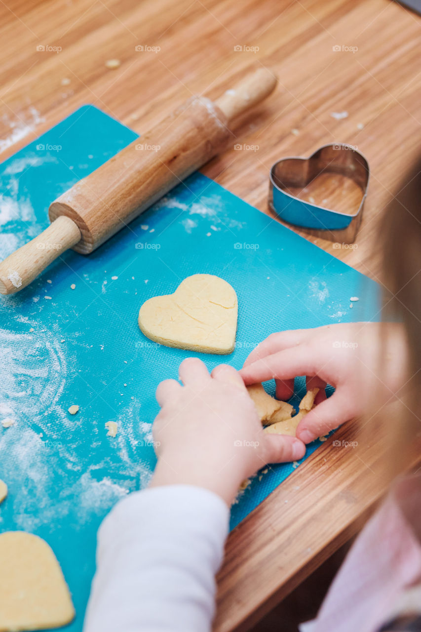 Little girl cutting the dough to heart shapes for the cookies. Kid taking part in baking workshop. Baking classes for children, aspiring little chefs. Girls learning to cook