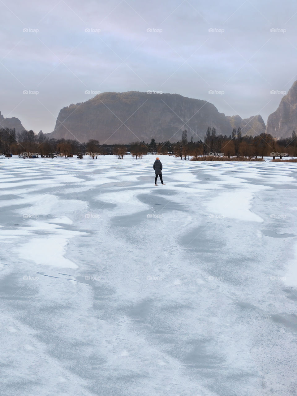 Tiny human walking by the frozen lake 