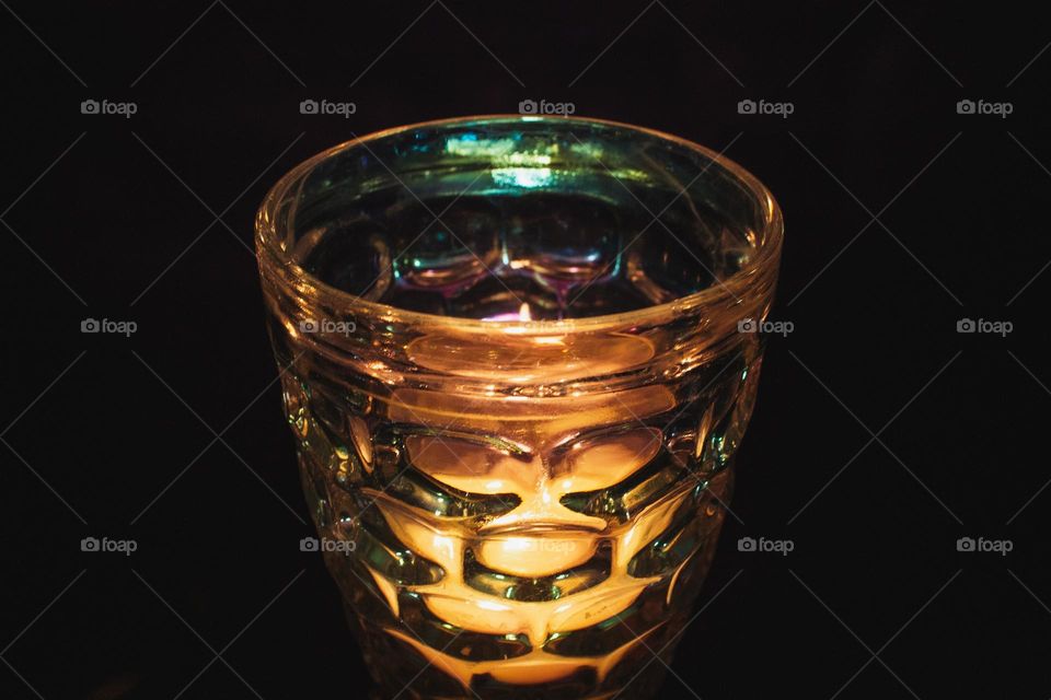 The flickering flame of a small candle through iridescent bubbled glass in the dark of night.