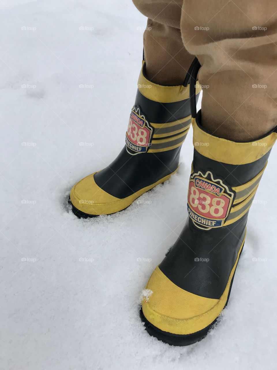 Child standing in snow with yellow rainboots