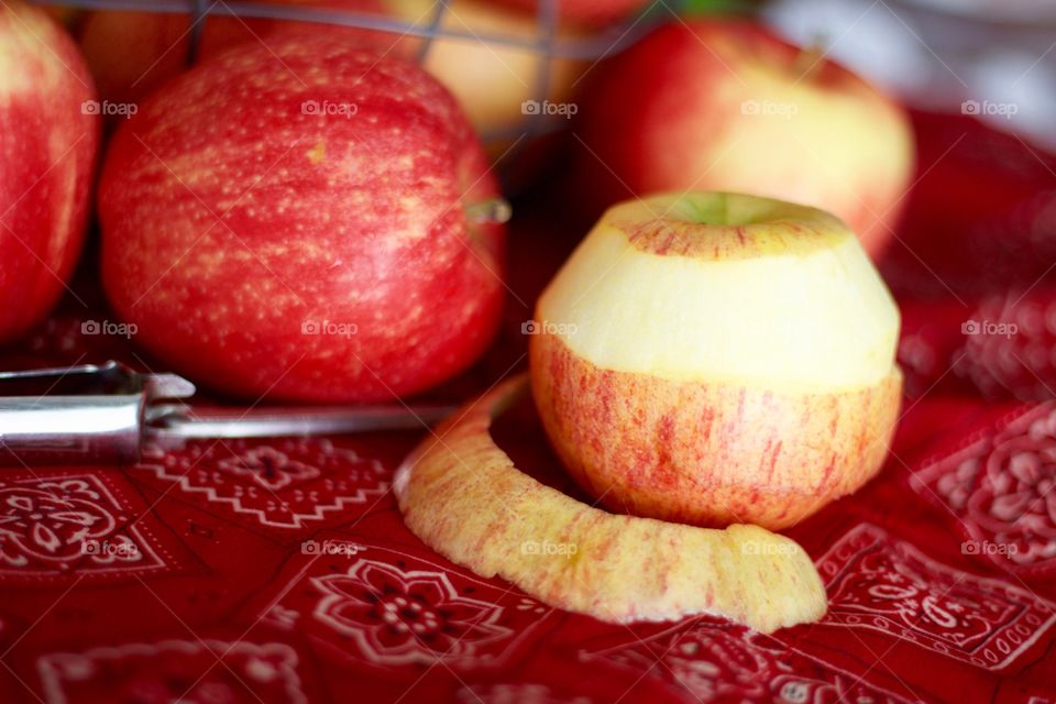 Fruits - Gala apples in a wire basket with a partially peeled apple and peeler on a red bandana-print tablecloth