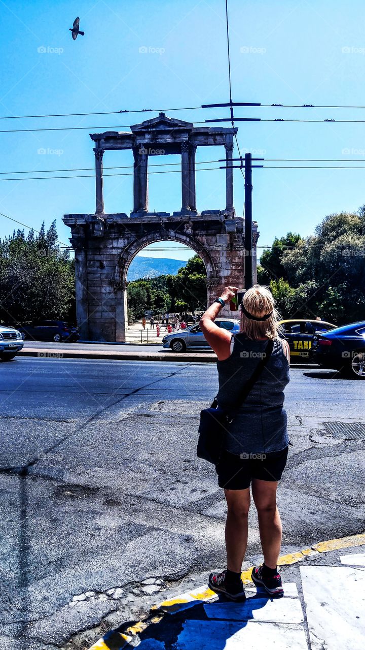 A tourist is taking a photo of Arch of Hadrian in Athens...Meanwhile a pigeon is flying
