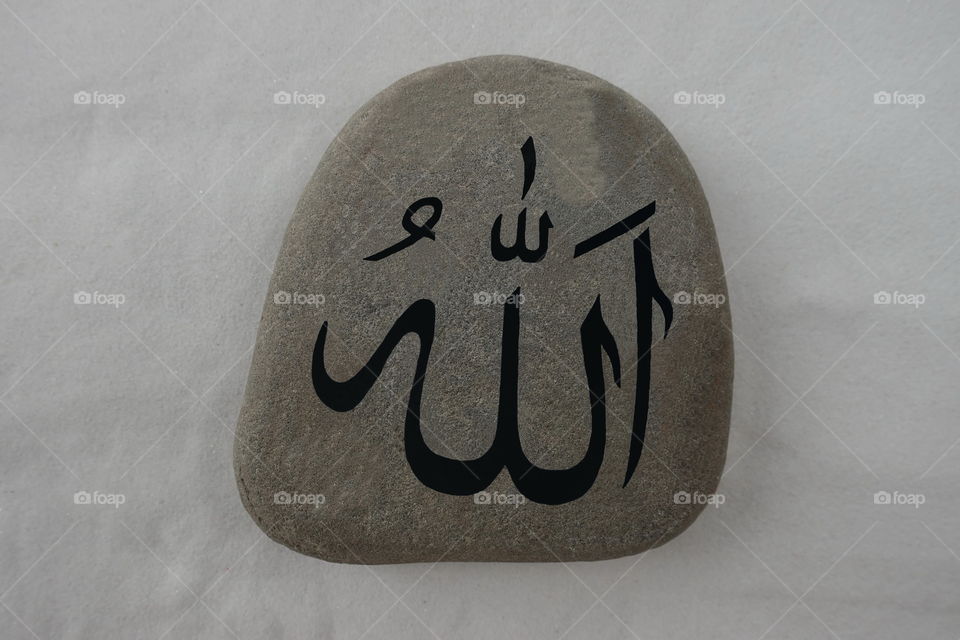 Allah word written on a stone over white sand
