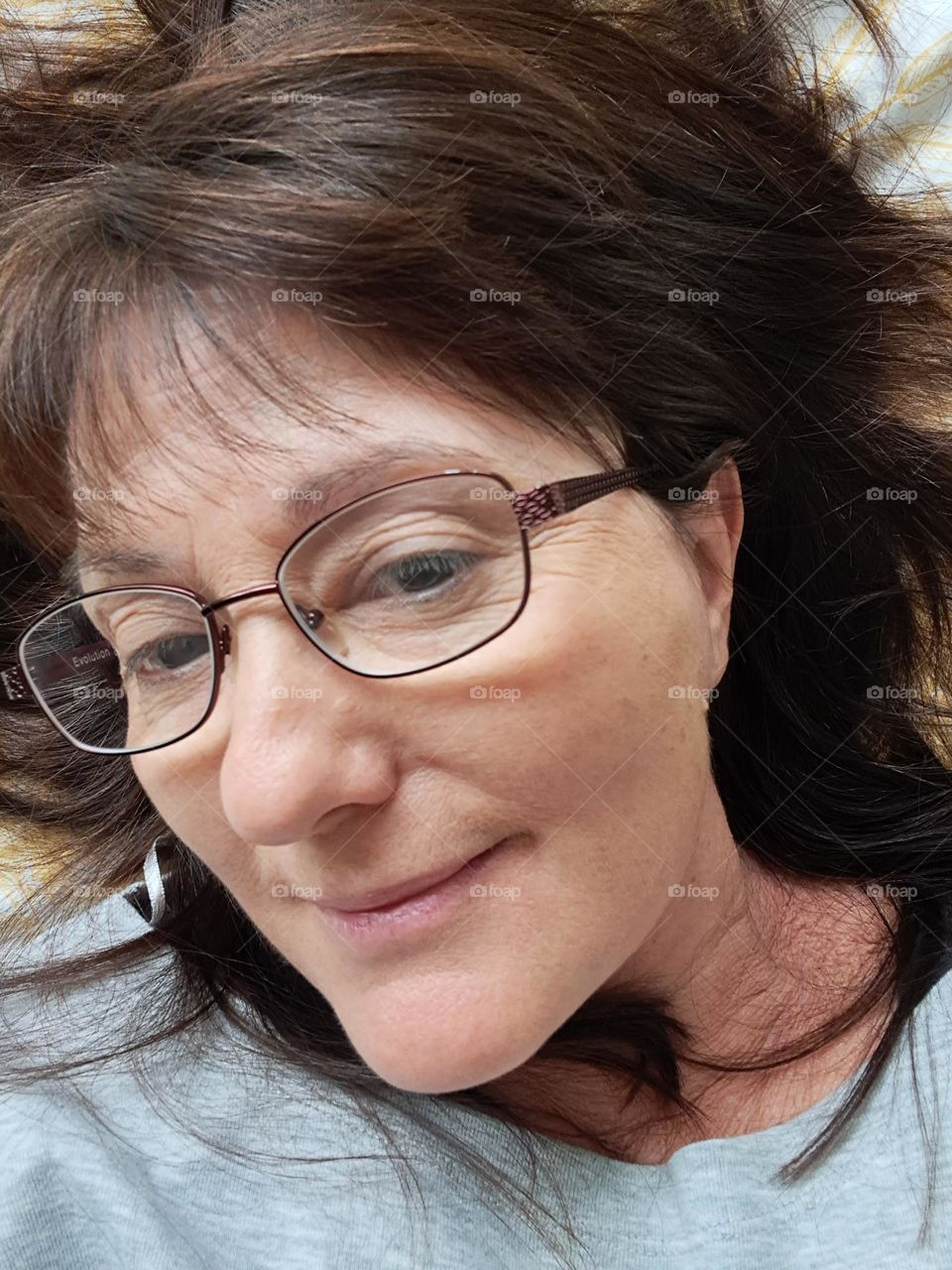 middleaged lady in glasses with long brown hair around her head as she lays to the side showing bare skin, a wart and her wrinkles!