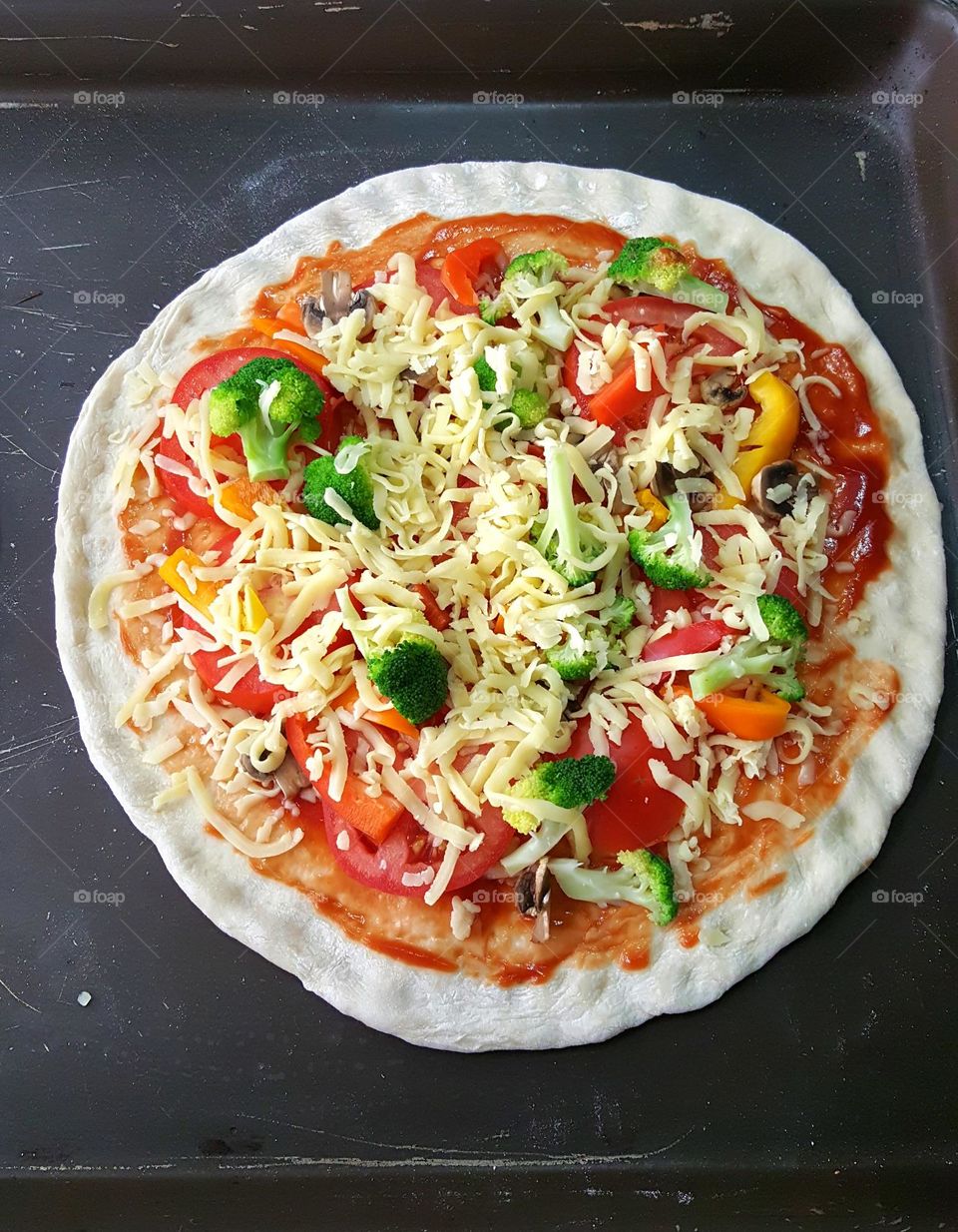 Artisanal pizza with tomato and broccoli and bell pepper and mozzarella being prepared for the oven