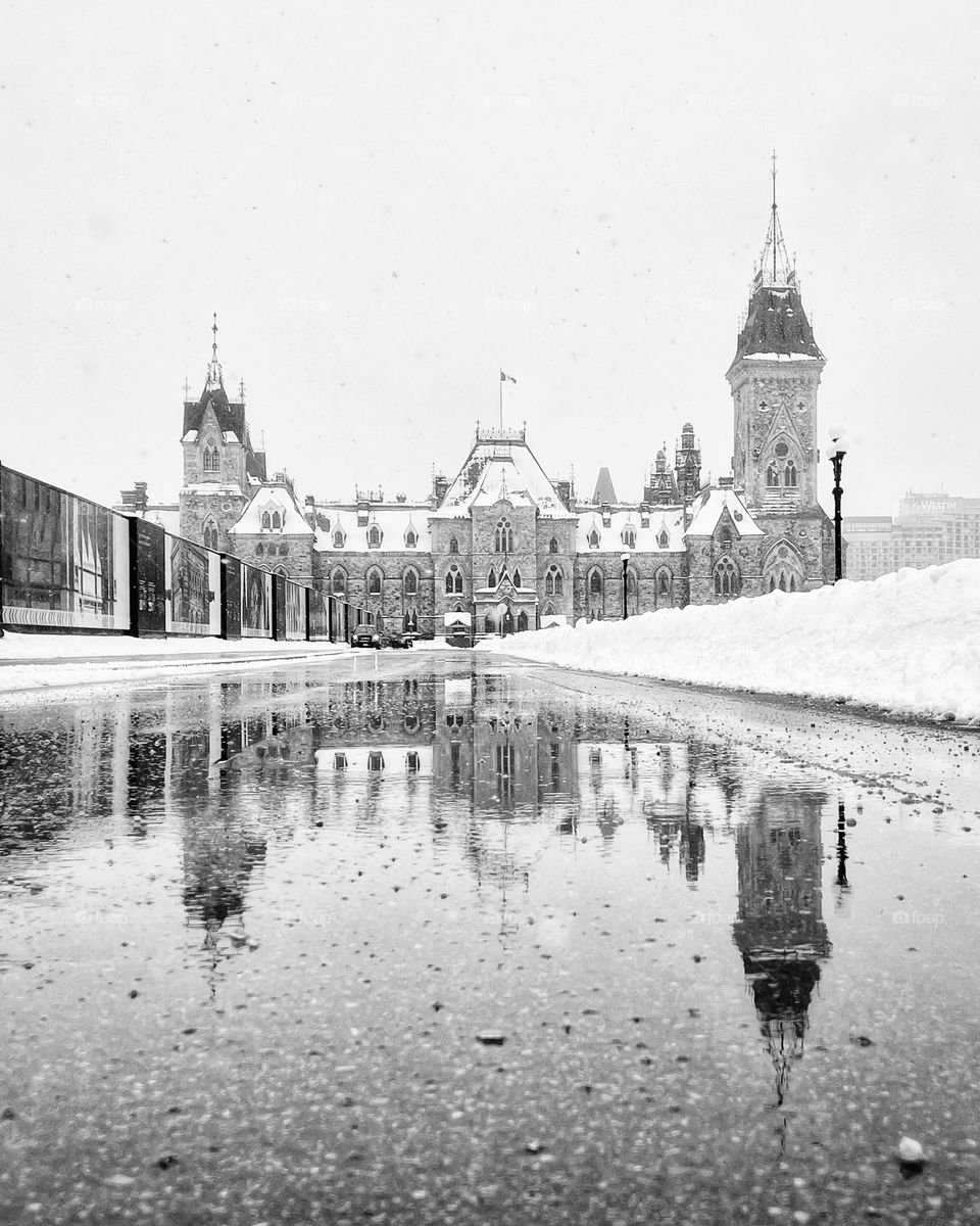 The parliament building in Canada’s capital Ottawa reflecting in a puddle with snow falling. 