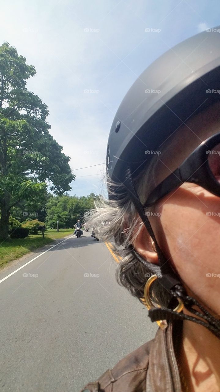 Countryside ride taking photo of other bikers behind motorcyclist. Pic taken holding camera over shoulder. Hot summer day, miles of road to ride on.