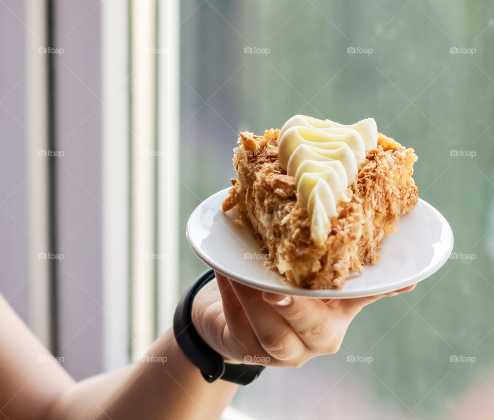 Piece of cake napoleon with whipped vanilla cream on the white plate in the persons hand.