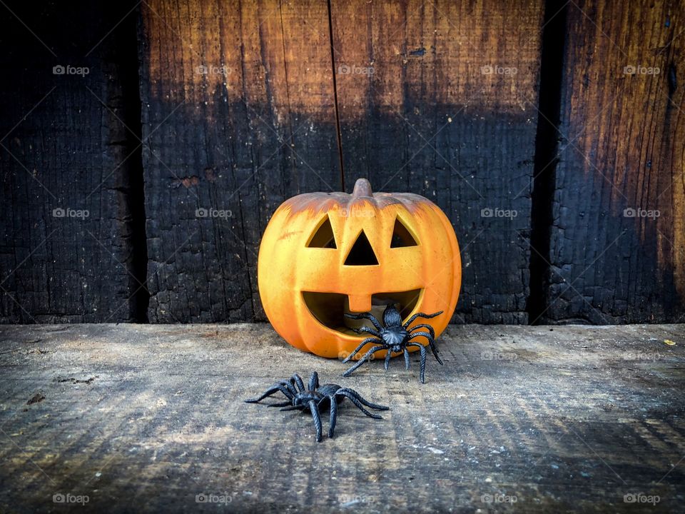 Scary pumpkin placed on rustic wooden table surrounded by big black decorative spiders