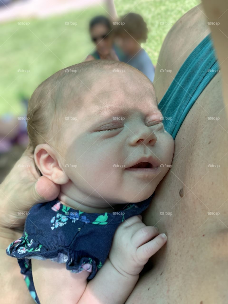 Smiling newborn baby being held in the shade on a summer day. 