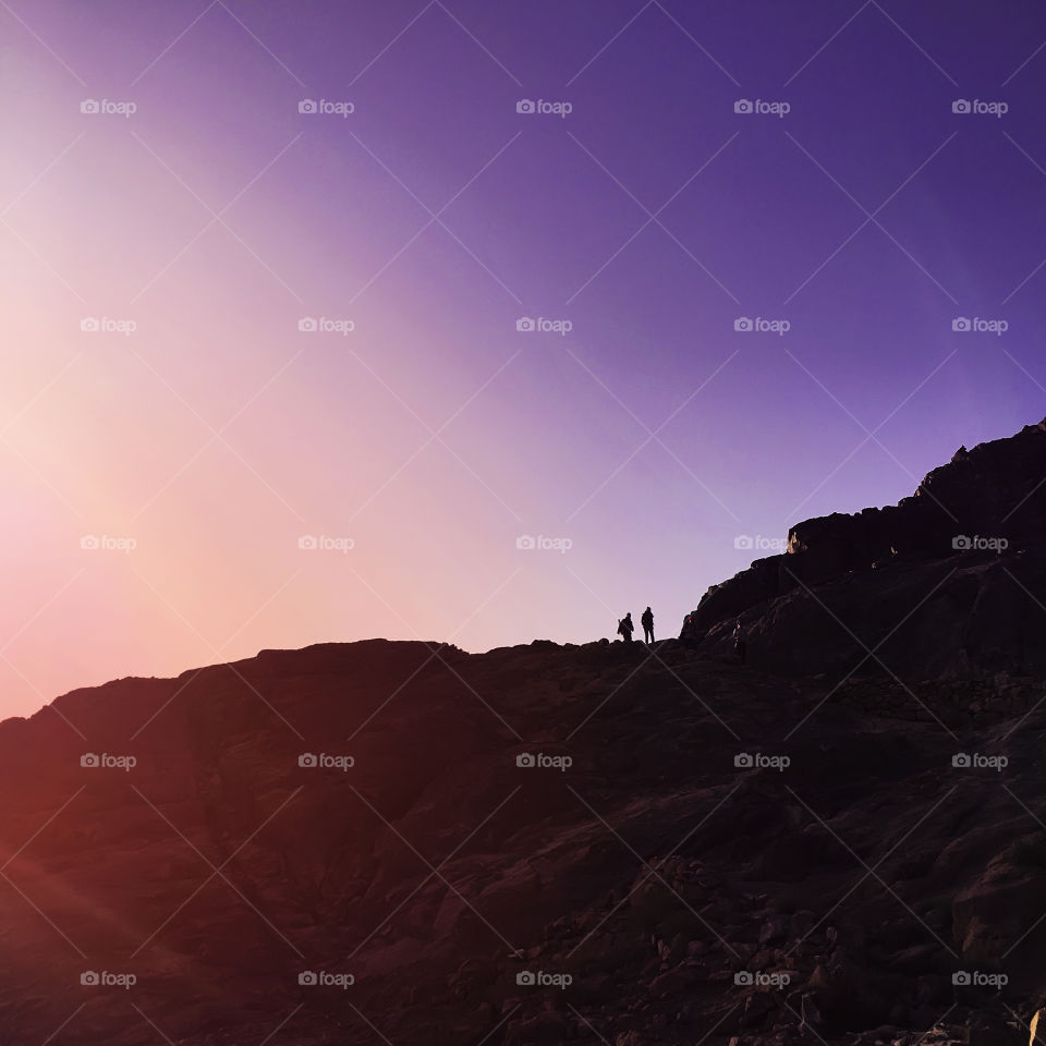 Two silhouettes hiking in mountains 