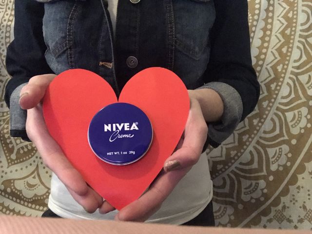 A woman holding a jar of Nivea cream and a red valentines heart wearing a denim blue jacket, Celebrating Valentine’s Day. USA, America