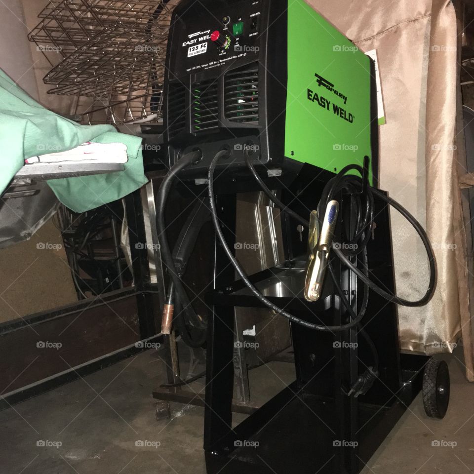 Forney FluxCore welder on a stand with wheels in a small welding shop.
