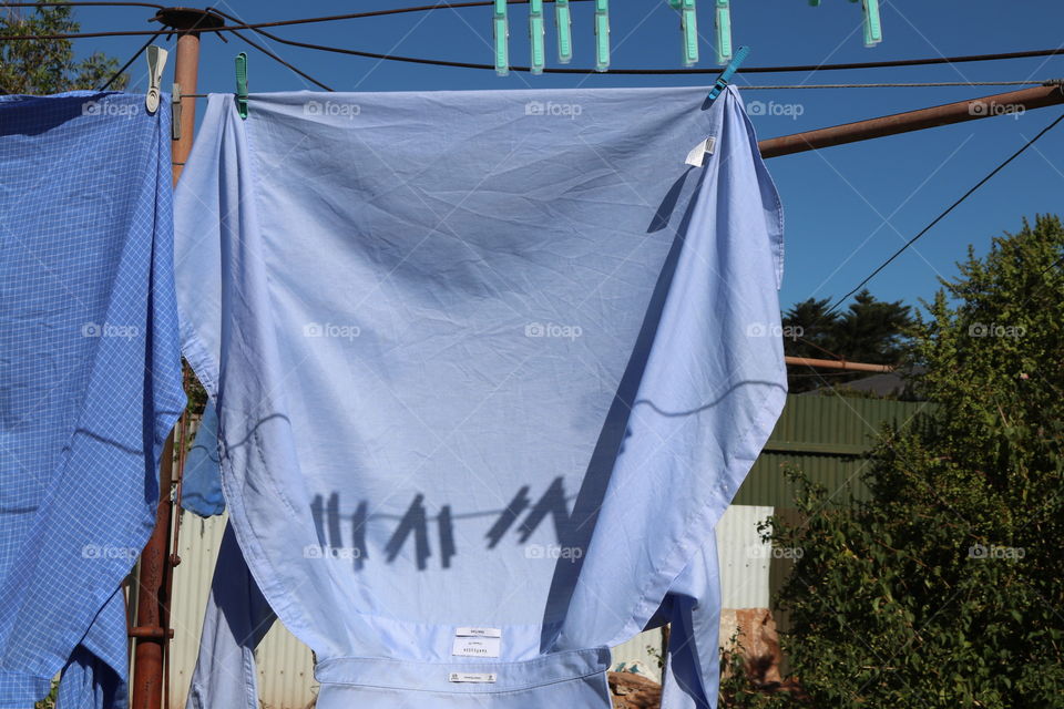 Shadow play on laundry hanging out to dry, man’s shirt on clothesline with clothespin shadows in the sunlight