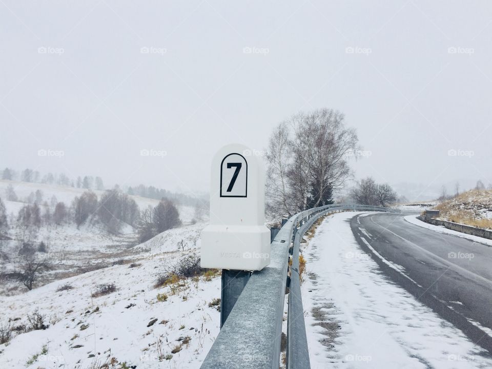 Stone mileage sign on a deserted road covered in snow during winter