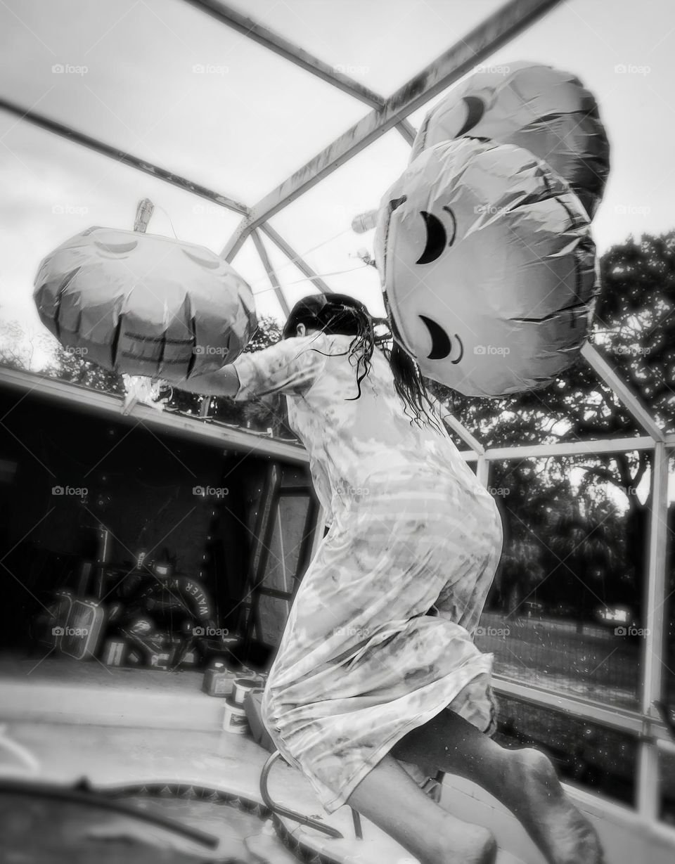 Smiley Faces Helium Balloons Seem To Pull The Girl Up In The Air While She Jumps In The Water With It In The Pool, In Black And White.